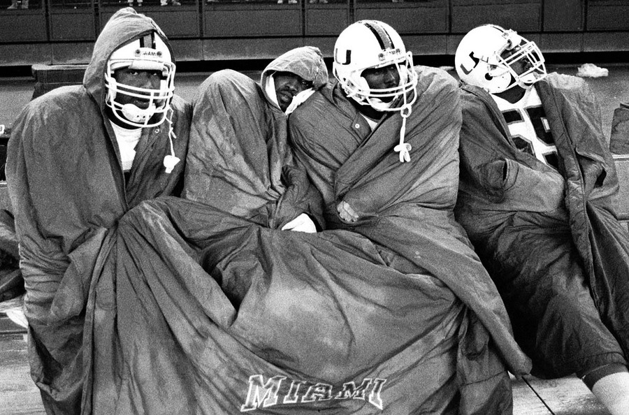 University of Miami players huddle under a blanket in cold rainy weather against Cincinnati in Riverfront Stadium in Cincinnati, Ohio. 