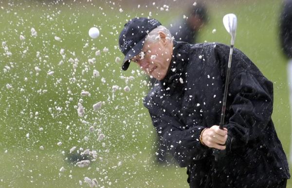 Former US President Bill Clinton practices hitting out of a sand trap in the rain before a tsunami relief golf fundraiser with golf pro Greg Norman and former president George H.W. Bush at the Medalist Golf Club in Hobe Sound,  Florida.