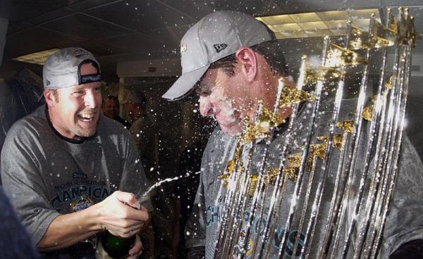 Florida Marlins players Mike Redmond (L) sprays Jeff Conine (R) with champagne as he holds the World Series Trophy in the locker room after defeating the New York Yankees 2-0 to win the World Series at Yankee Stadium in New York, New York.