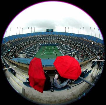 Fans sit under an umbrella in the upper deck of Arthur Ashe Stadium during a rain delay at the US Open in Flushing Meadows, NY